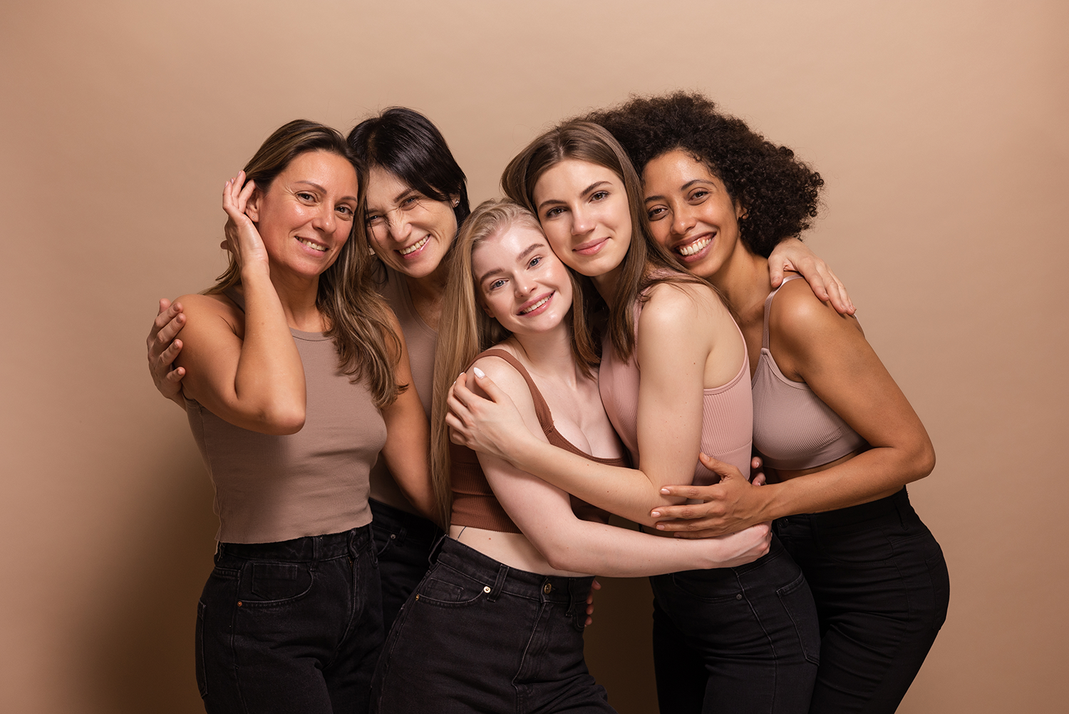 five-pretty-african-caucasian-women-brown-tops-black-jeans-look-camera-beige-background